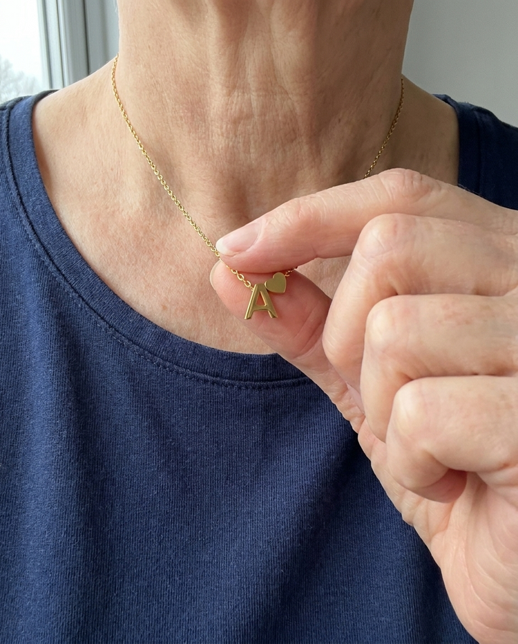 Customer wearing an initial and heart necklace in gold